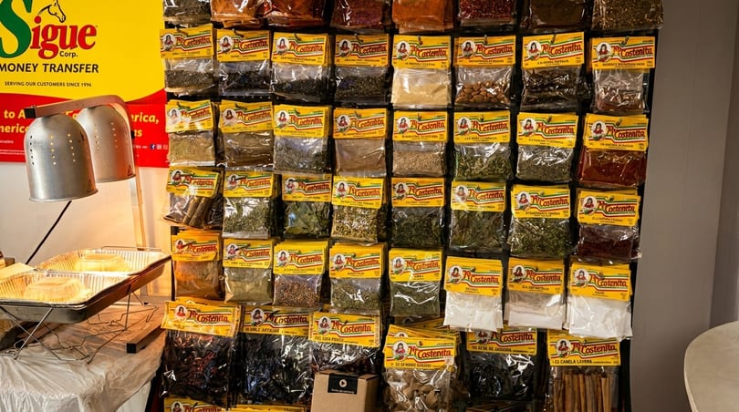 A wall display of various spices and herbs in small clear bags with yellow labels, next to a food warmer.